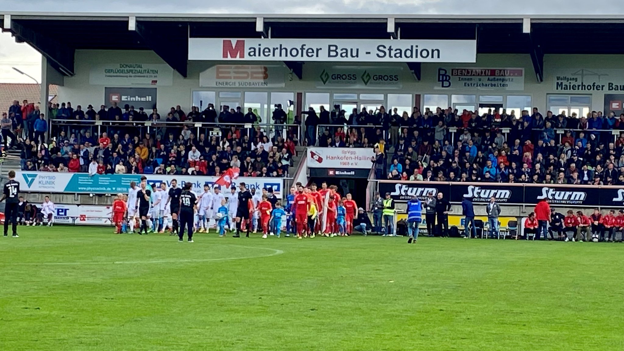 Spieler und vollbesetzte Zuschauertribüne im Maierhofer-Bau-Stadion in Hankofen