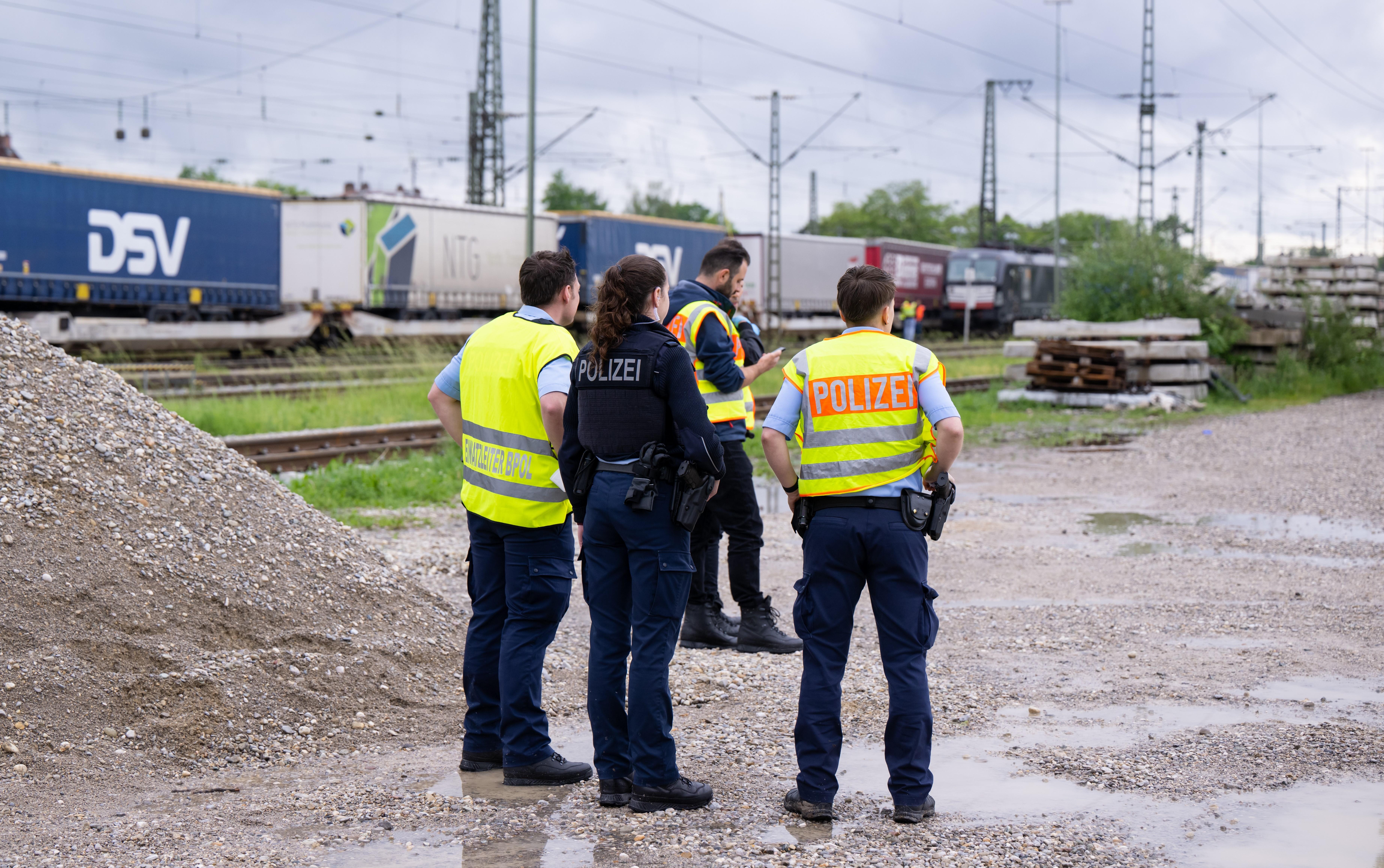 Drei Polizisten und eine Polizistin stehen in München-Trudering auf einer Kiesfläche neben Gleisen; auf einem davon steht ein Güterzug. Eine 15-Jährige starb an einem Stromschlag, als sie nach ihrer Flucht von dem Zug kletterte. Archivbild vom 24. Mai 2022. 