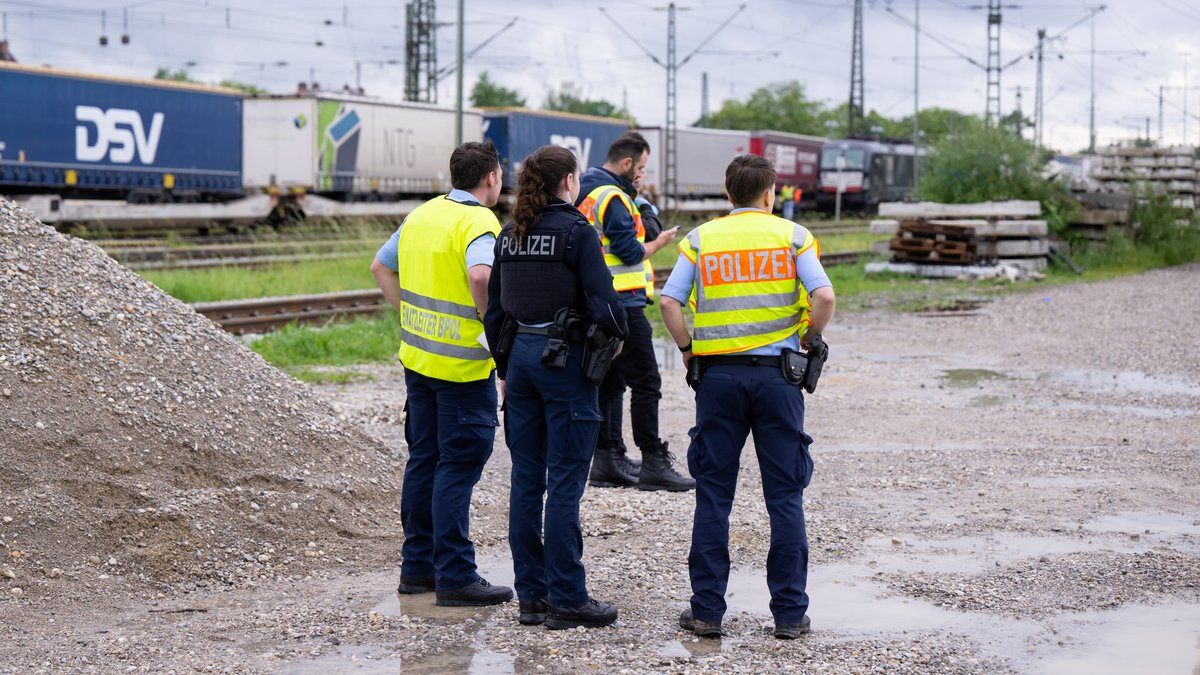 Drei Polizisten und eine Polizistin stehen in München-Trudering auf einer Kiesfläche neben Gleisen; auf einem davon steht ein Güterzug. Eine 15-Jährige starb an einem Stromschlag, als sie nach ihrer Flucht von dem Zug kletterte. Archivbild vom 24. Mai 2022. 