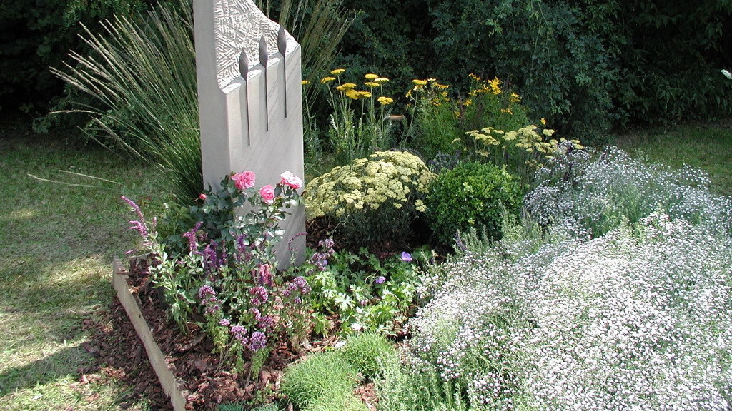 Grab mit weißem Grabstein und vielen blühenden Pflanzen