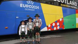 Drei Jungen in bayerischer Tracht stehen vor dem schottischen Mannschaftsbus.  | Bild:BR / Alisa Schröter