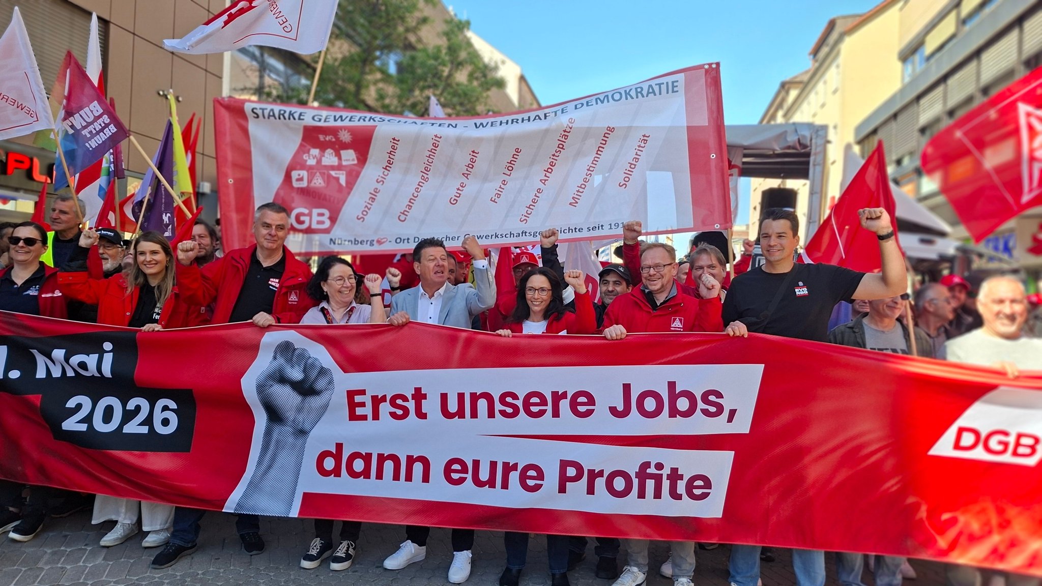Führende Gewerkschafter ziehen mit einem Banner durch Nürnberg. Darauf steht "Erst unsere Jobs, dann eure Profite".