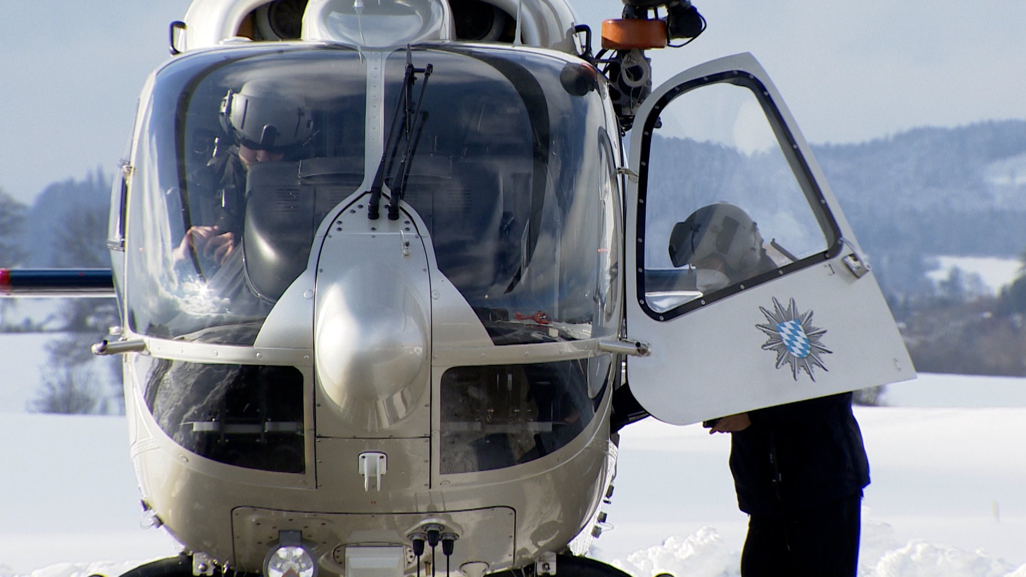 Ein Polizeihubschrauber am Boden, ein Polizist sitzt im Hubschrauber, ein anderer steht in der offenen Tür