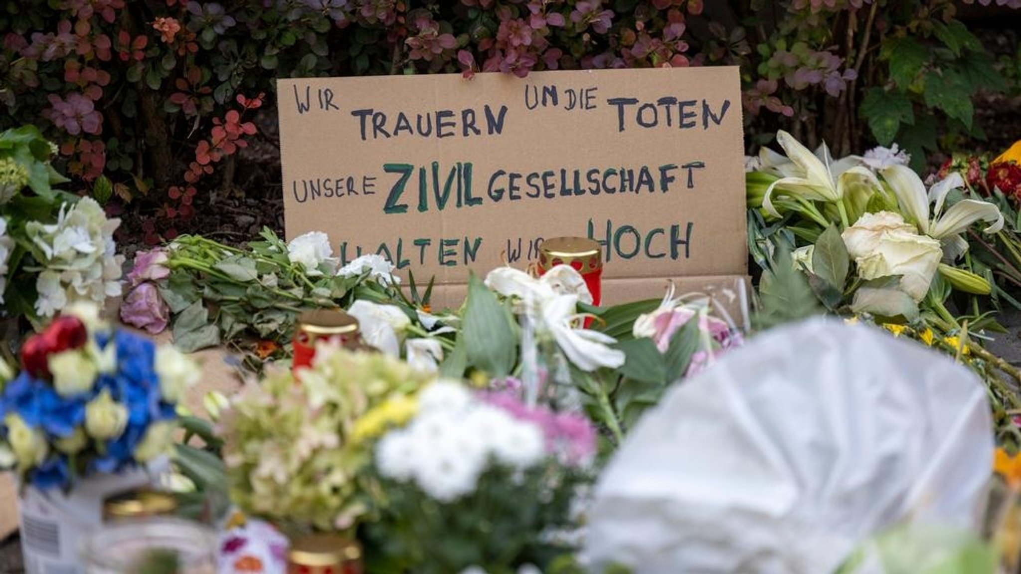 26.08.2024, Nordrhein-Westfalen, Solingen: In der Nähe des Tatorts haben Menschen Blumen, Kerzen und auf Schildern gemalte Botschaften niedergelegt. Auf einem Schild steht "Wir trauern um die Toten -  Unsere Zivilgesellschaft halten wir hoch".  Bei einer Messerattacke auf der 650-Jahr-Feier der Stadt Solingen am 23. August hatte es Todesopfer und Verletzte gegeben. Foto: Thomas Banneyer/dpa +++ dpa-Bildfunk +++