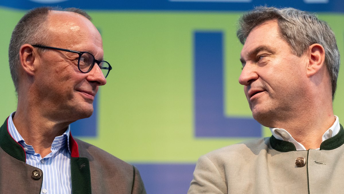 ARCHIV (04.09.2023): Markus Söder (r., CSU), Ministerpräsident von Bayern, und Friedrich Merz, Bundesvorsitzender der CDU, stehen beim Politischen Frühschoppen Gillamoos auf der Bühne und schauen sich an. 