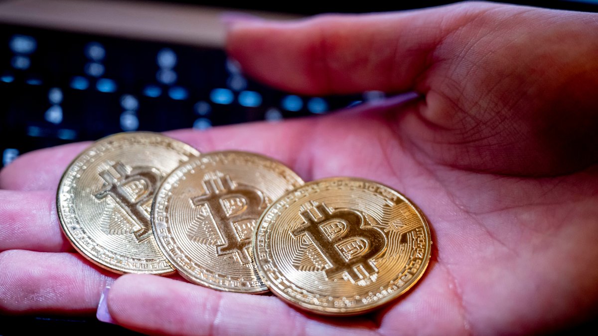 Drei Bitcoin-"Münzen" liegen auf einer Hand, dahinter eine Computertastatur