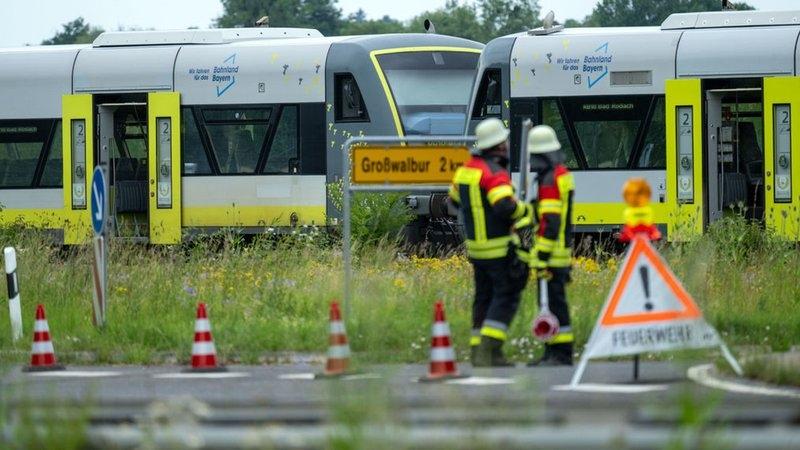Feuerwehrleute stehen vor einem Bahnübergang, an dem ein Zug angehalten hat. 