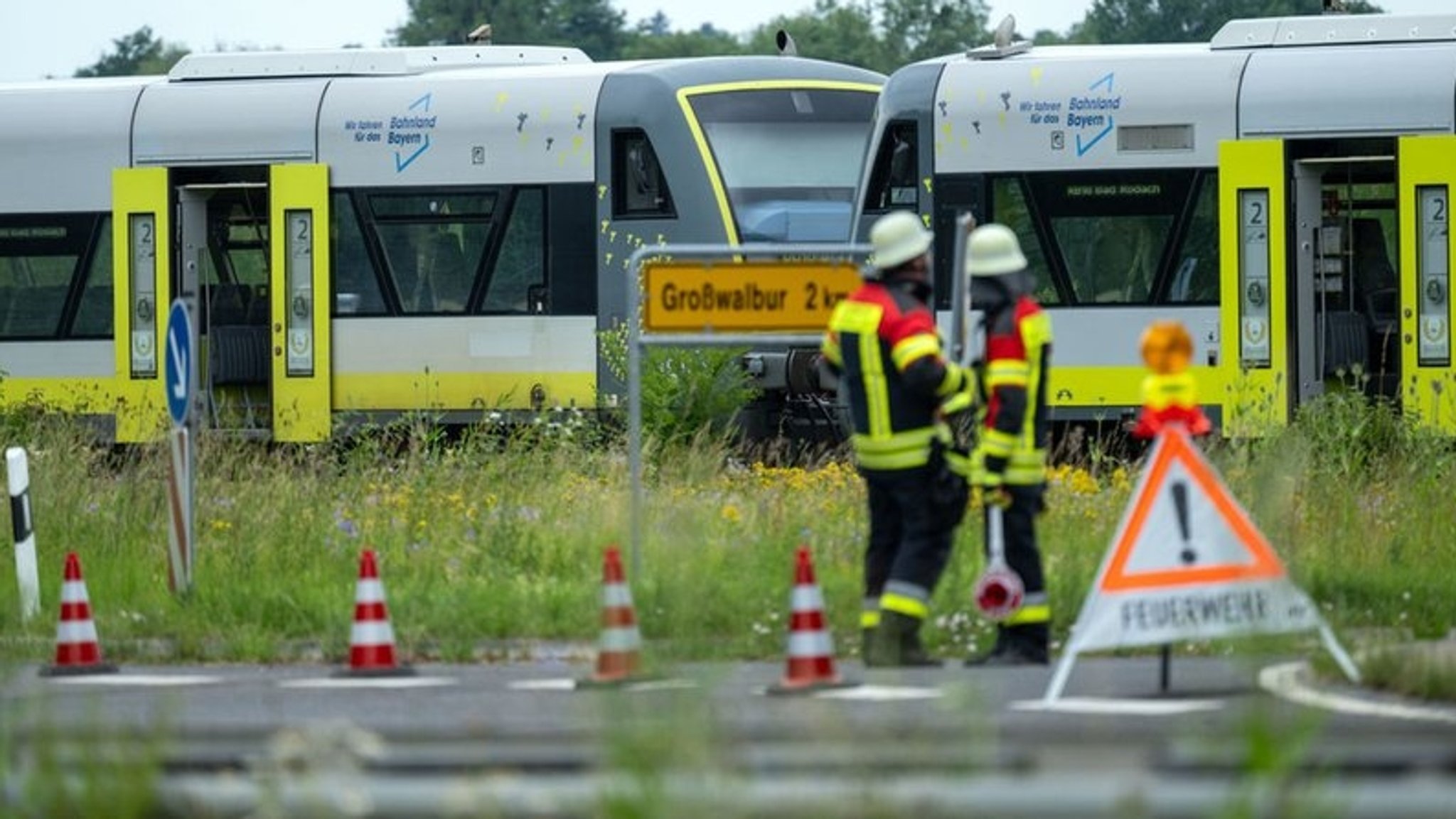 Feuerwehrleute stehen vor einem Bahnübergang, an dem ein Zug angehalten hat. 