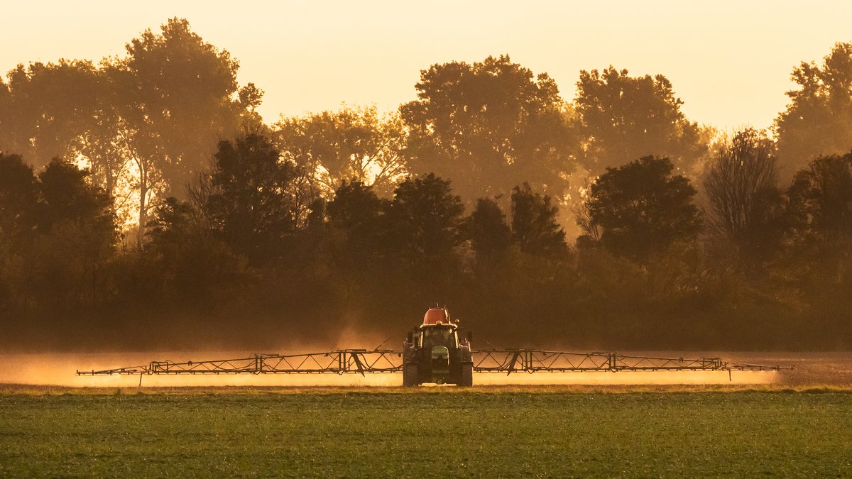 Ein Bauer versprüht mit seinem Traktor Chemie auf seinem Feld.