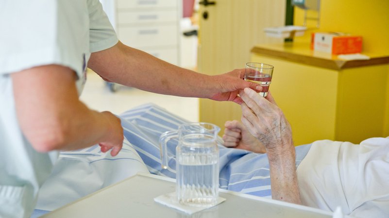 Eine Krankenpflegerin reicht einem Patienten ein Glas Wasser. Hitzeperioden sind gerade für Alte und Kranke gefährlich. | Bild: dpa-Bildfunk/Daniel Karmann Eine Krankenpflegerin reicht einem Patienten ein Glas Wasser. Hitzeperioden sind gerade für Alte und Kranke gefährlich.