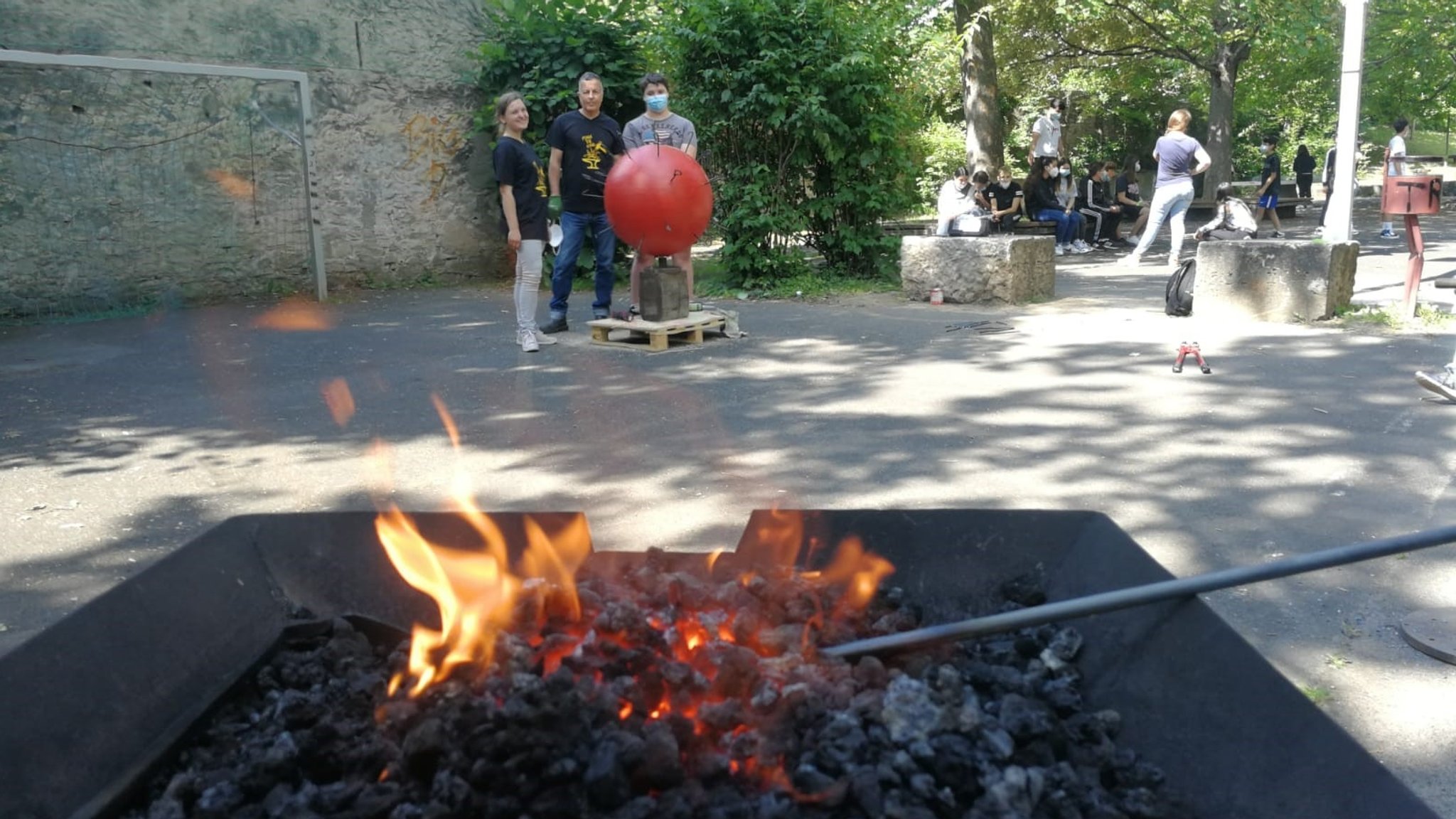 Eisenstangen werden in der Glut erhitzt, im Hintergrund die Corona-Kunst der Schüler der D.-Paul-Eber-Schule in Kitzingen