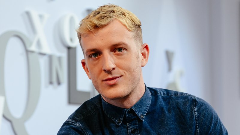 Porträt des französischen Schriftstellers Édouard Louis, er sitzt vor einer mit Buchstaben geschmückten blau-grauen Wand | Bild: picture alliance / Jan Haas | Jan Haas Porträt des französischen Schriftstellers Édouard Louis, er sitzt vor einer mit Buchstaben geschmückten blau-grauen Wand