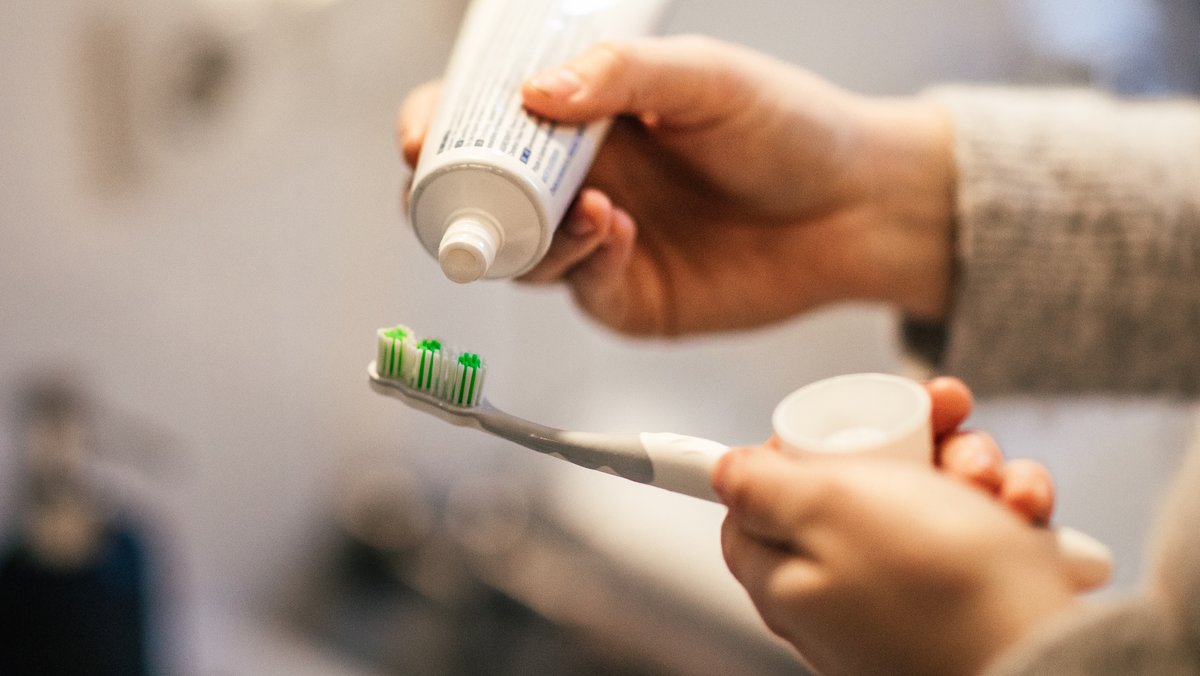 Eine Frau schmiert in einem Bad Zahnpasta auf eine Zahnbürste.