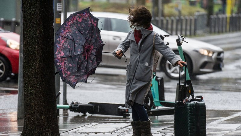Eine Frau kämpft mit dem stürmischen Wind, während sie versucht, eine Straße zu überqueren. 