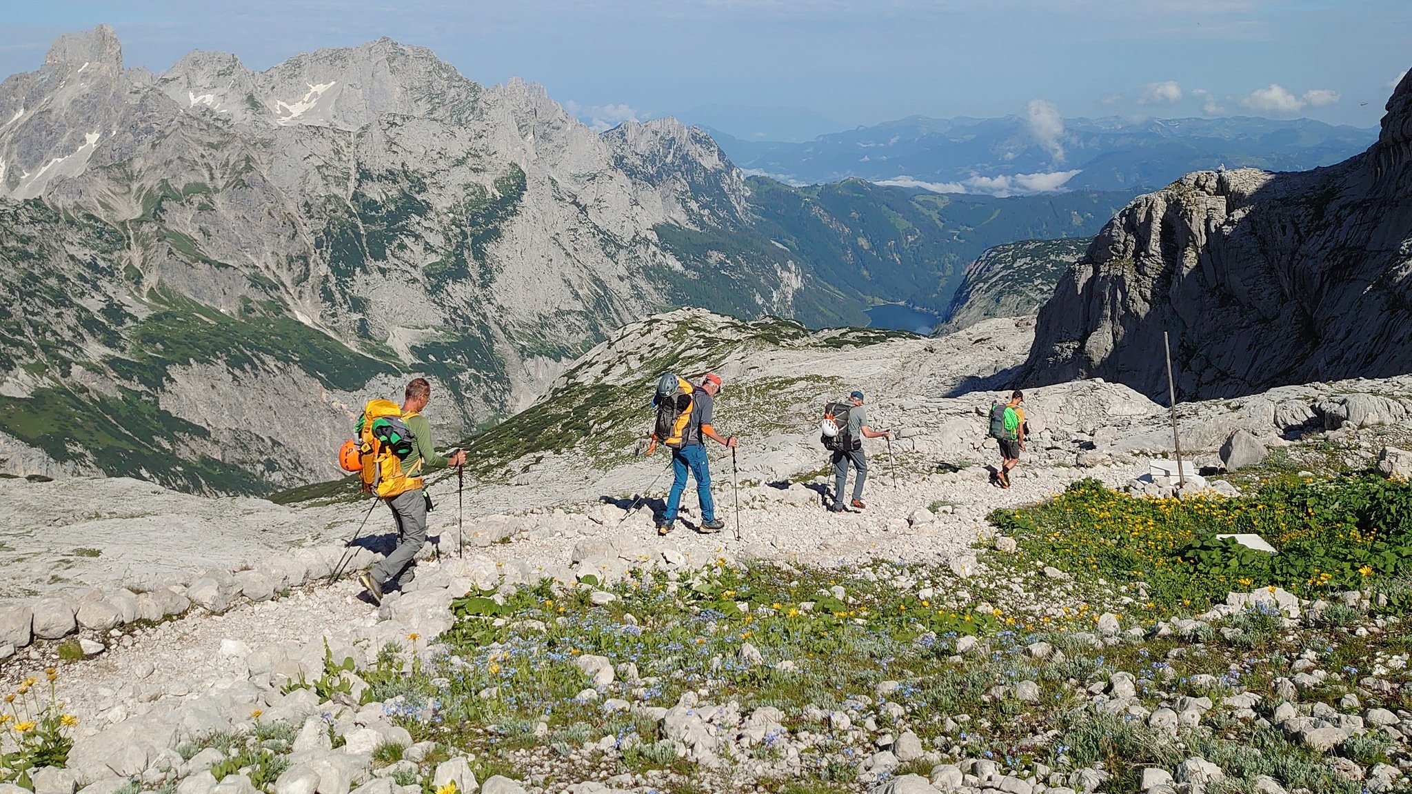 Vier Männer von der DAV Sektion Hof wandern auf einem steinigen Pfad am Dachstein. Im Hintergrund sieht man den Gosaukamm.