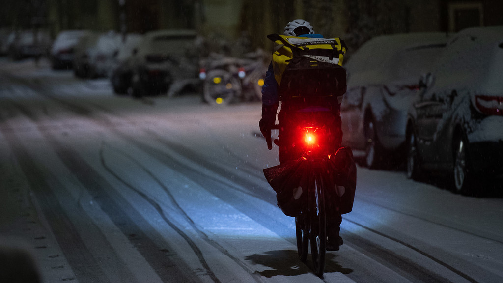 Ein Radfahrer fährt im Dunkeln über eine verschneite Straße.