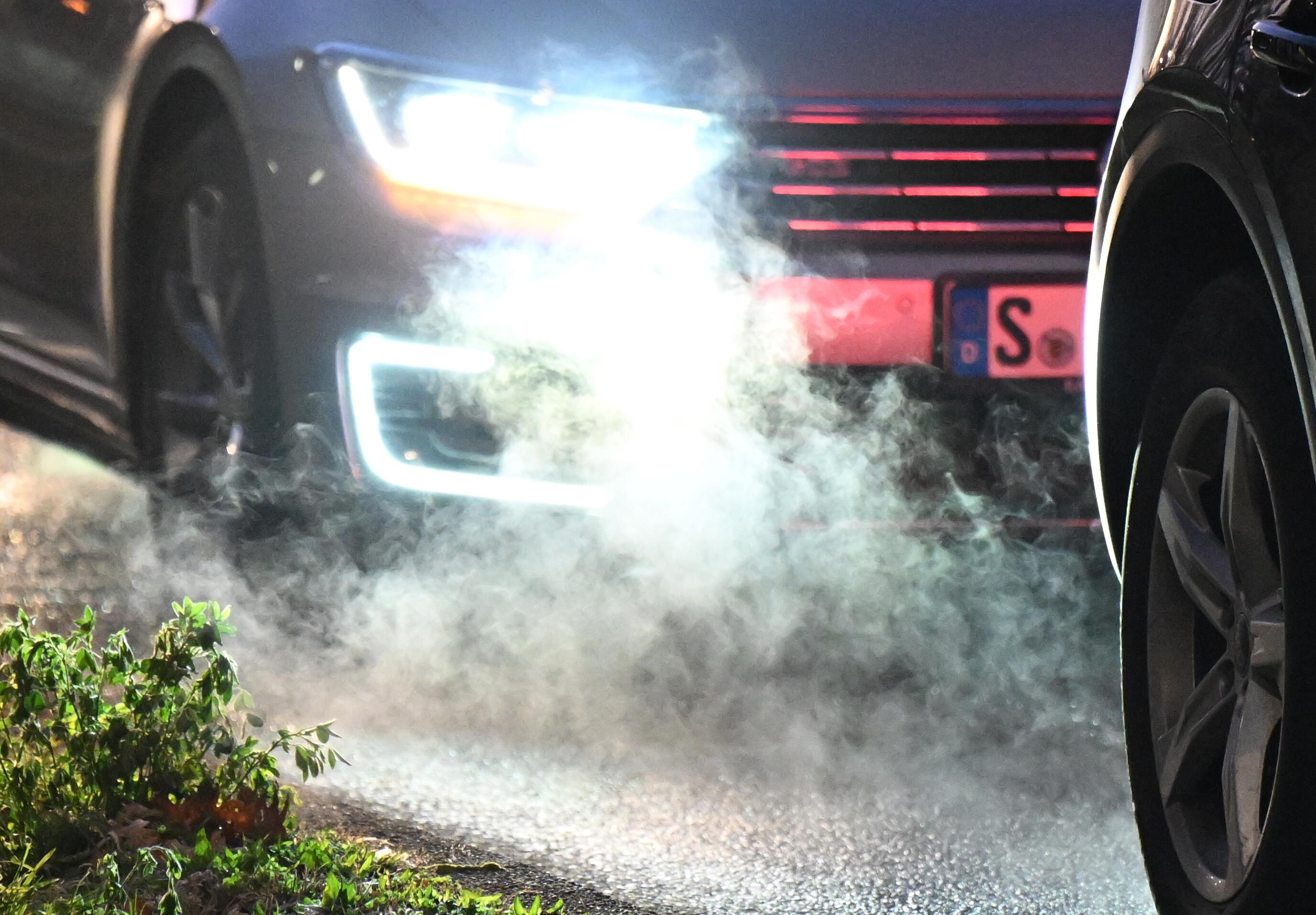 Zwei Autos stehen auf der Straße, während die Abgase vom Frontschweinwerfer des hinteren Fahrzeugs beleuchtet werden.