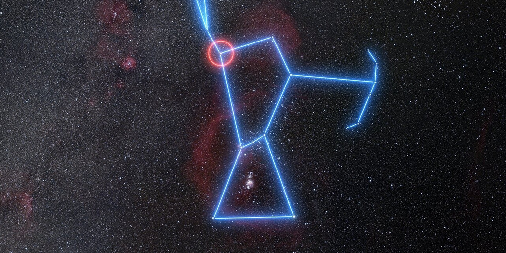Die Weitwinkelansicht zeigt die Himmelsregion voller Sterne rund um das Sternbild Orion. Orion selbst ist mit blau leuchtenden Linien nachgezeichnet, Beteigeuze ist als Schulterstern mit einem roten Kreis markiert. 