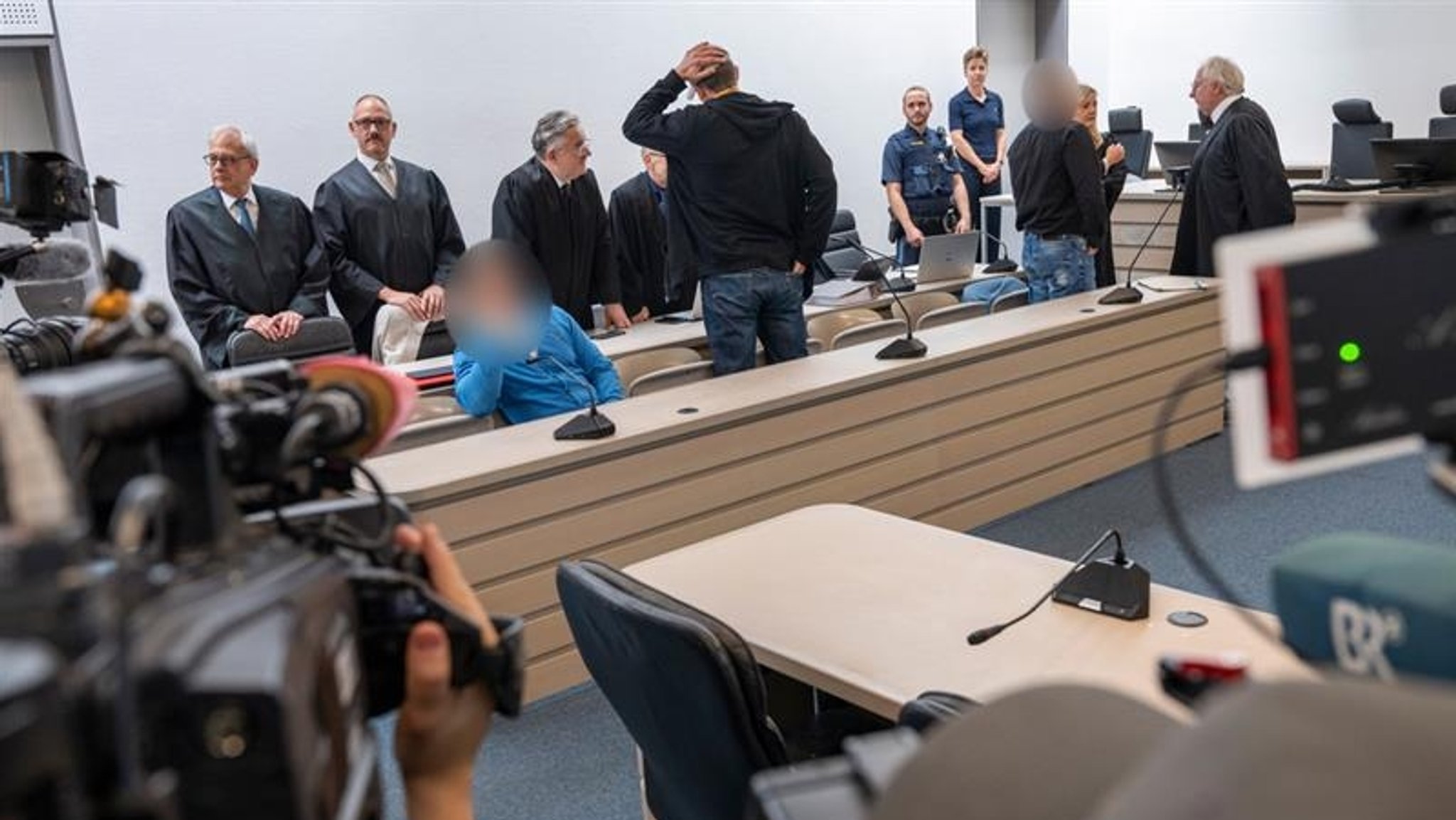 Der Gerichtssaal am Landgericht Ingolstadt ist vollbesetzt, hinten den Angeklagten stehen ihre Verteidiger. Fernsehteams filmen sie.