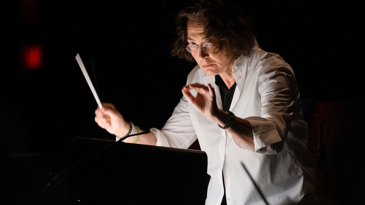 Die Dirigentin Nathalie Stutzmann steht mit einem Taktstock in der Hand am Pult und dirigiert. 