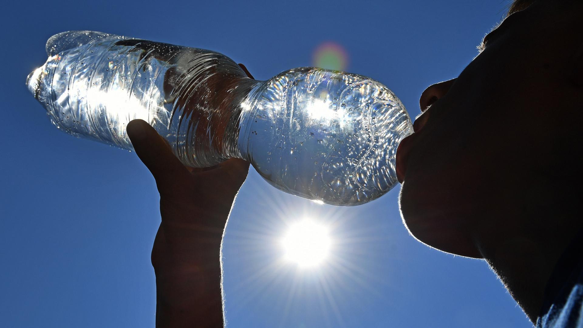 Junge trinkt Wasser aus einer Flasche bei grosser Hitze. Besonders an heißen Sommertagen müssen wir ausreichend Flüssigkeit zu uns nehmen. Wir erklären euch wieviel, wie ihr es schafft bei Hitze ausreichend zu trinken und zu welchen Durstlöschern ihr greifen solltet. 