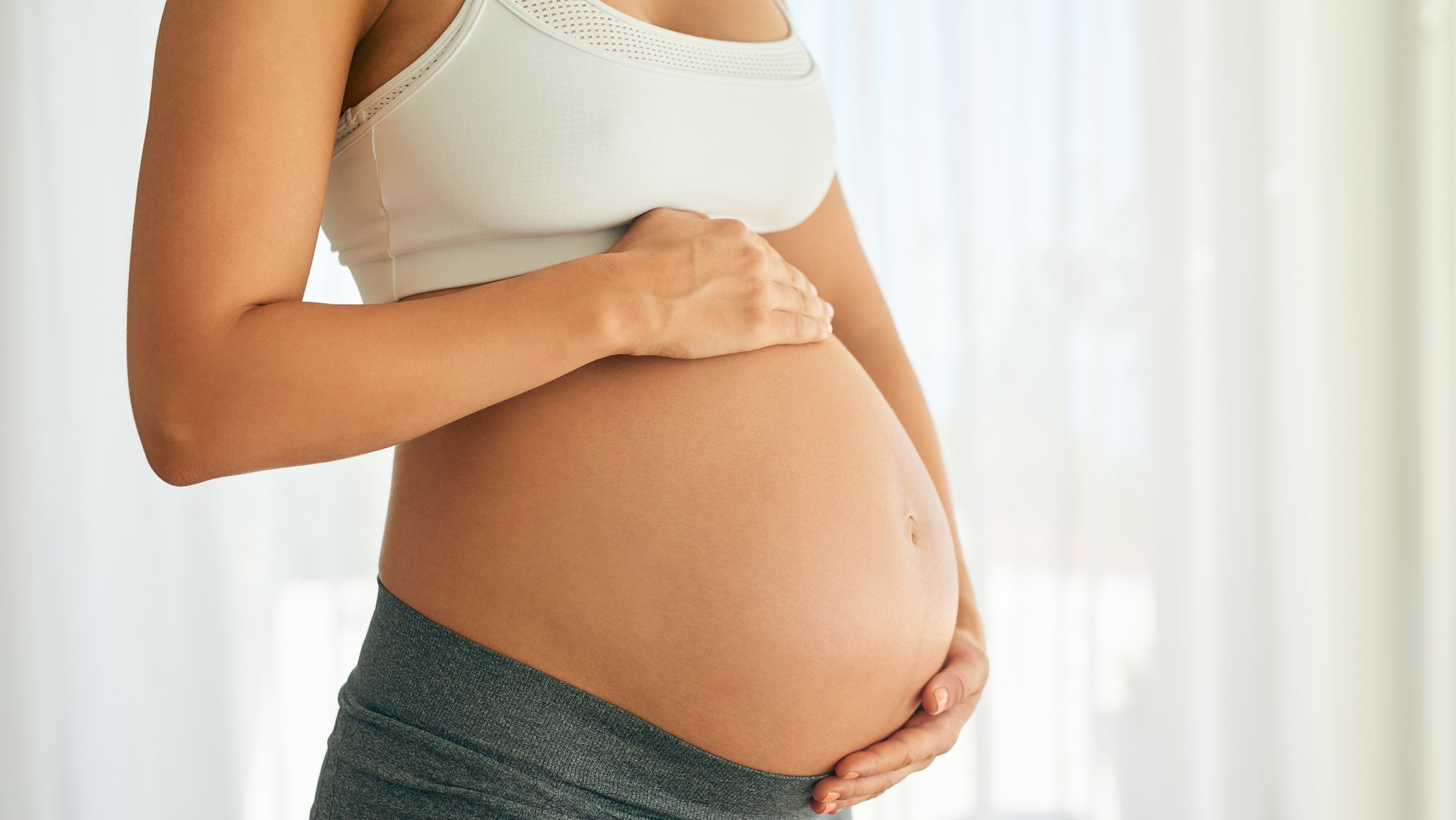 Schwangere Frau hält Hände auf ihren runden Baby-Bauch.