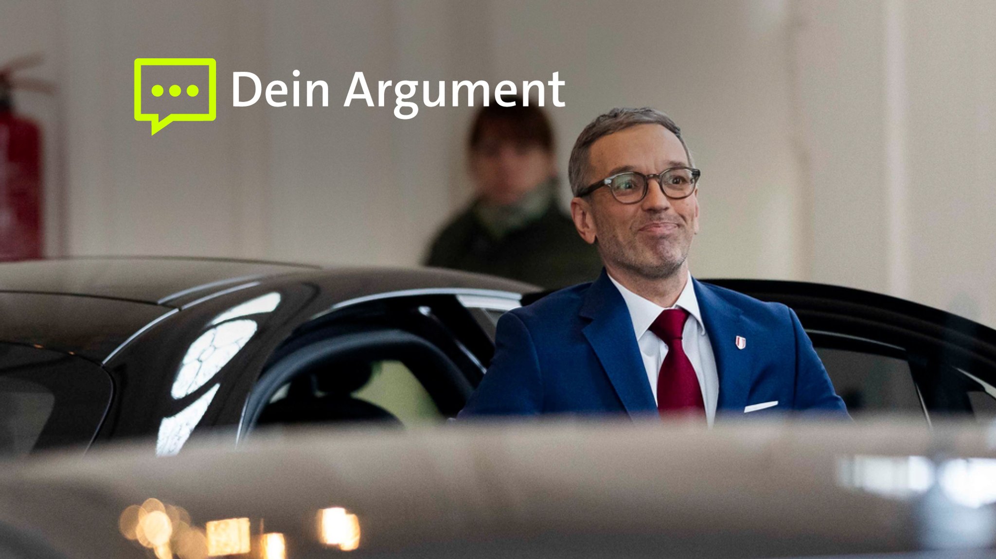 Herbert Kickl steht vor einem Auto und grinst. 