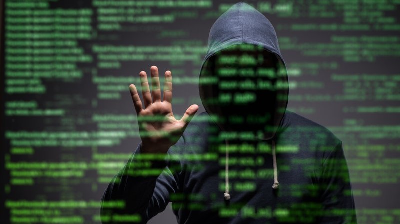 Nicht erkennbarer junger Hacker mit Kapuzenjacke im Dunkeln hält Hand an unscharfe grüne Schriften eines vermeintlichen Datensicherheitskonzeptes. | Bild: colourbox.de/Elnur Amikishiyev Nicht erkennbarer junger Hacker mit Kapuzenjacke im Dunkeln hält Hand an unscharfe grüne Schriften eines vermeintlichen Datensicherheitskonzeptes.