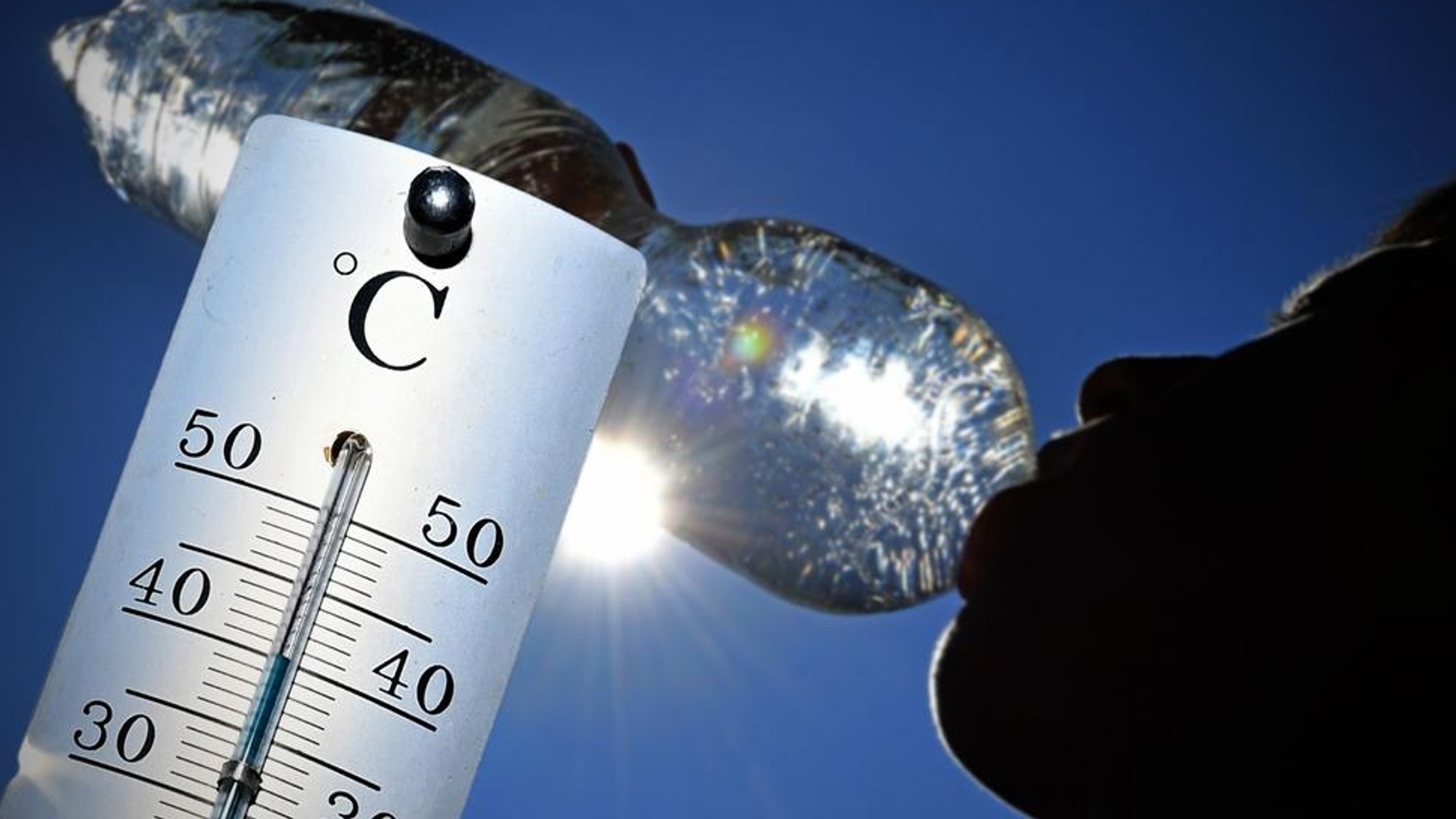 Hitze in Bayern: Ein Thermometer zeigt Temperaturen über 30 Grad und eine Person, die aus einer Wasserflasche trinkt  (Symbolbild)