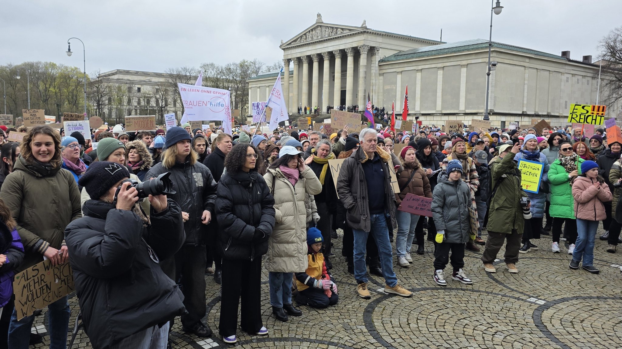 Auf dem Münchner Königsplatz stehen Demonstrantinnen und Demonstranten mit Schildern und Fahnen. Auf einem der Schilder ist zu lesen: "Es reicht!"