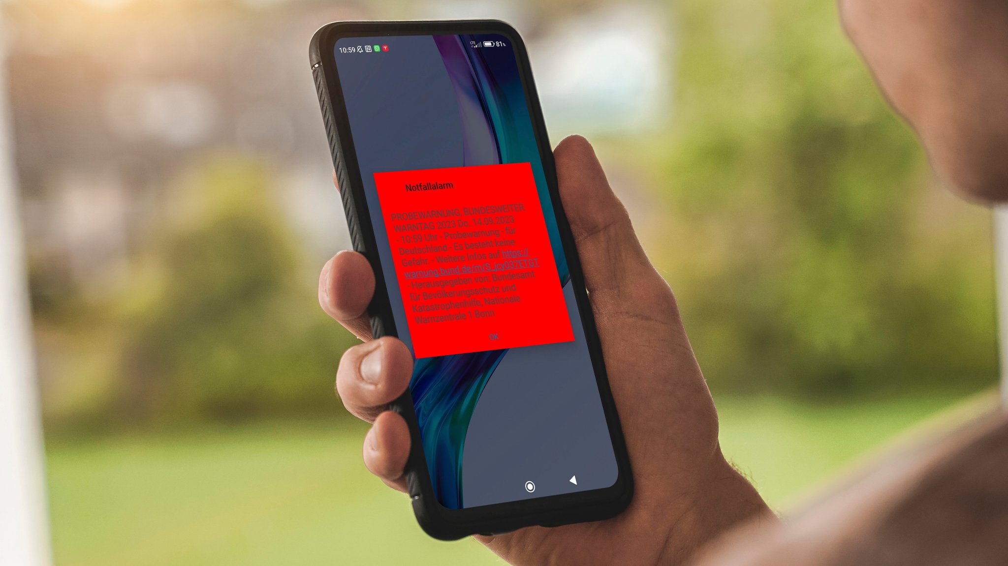 Ein Mann hält ein Handy mit Warn-Text