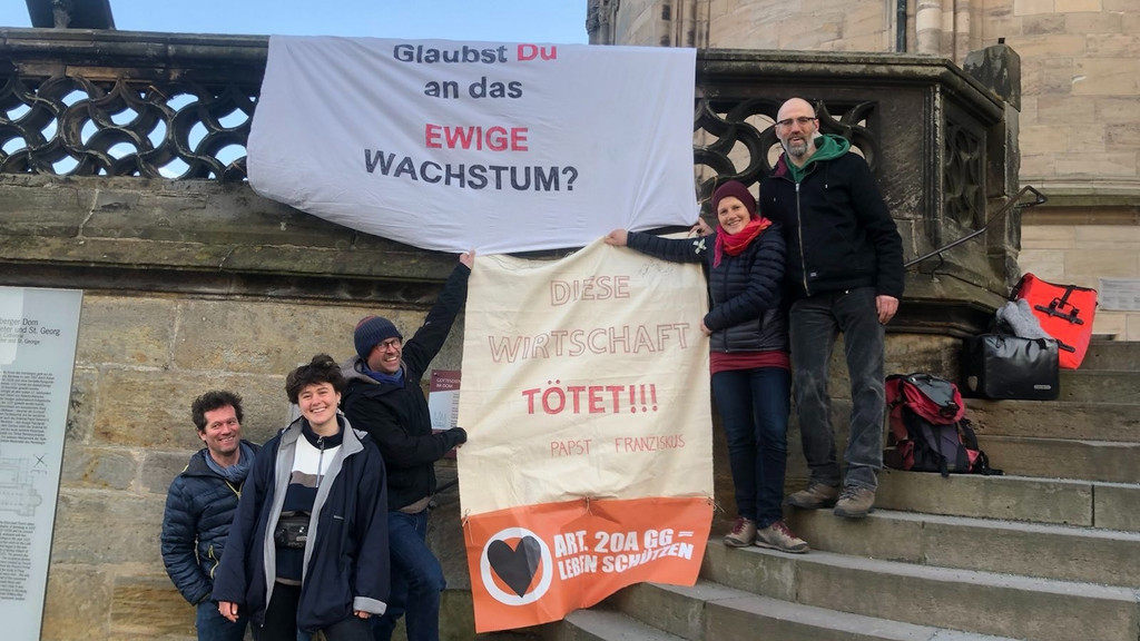 Aktivisten stehen mit einem Plakaten vor dem Bamberger Dom, auf denen unter anderem zu lesen ist: Glaubst Du an das ewige Wachstum? 