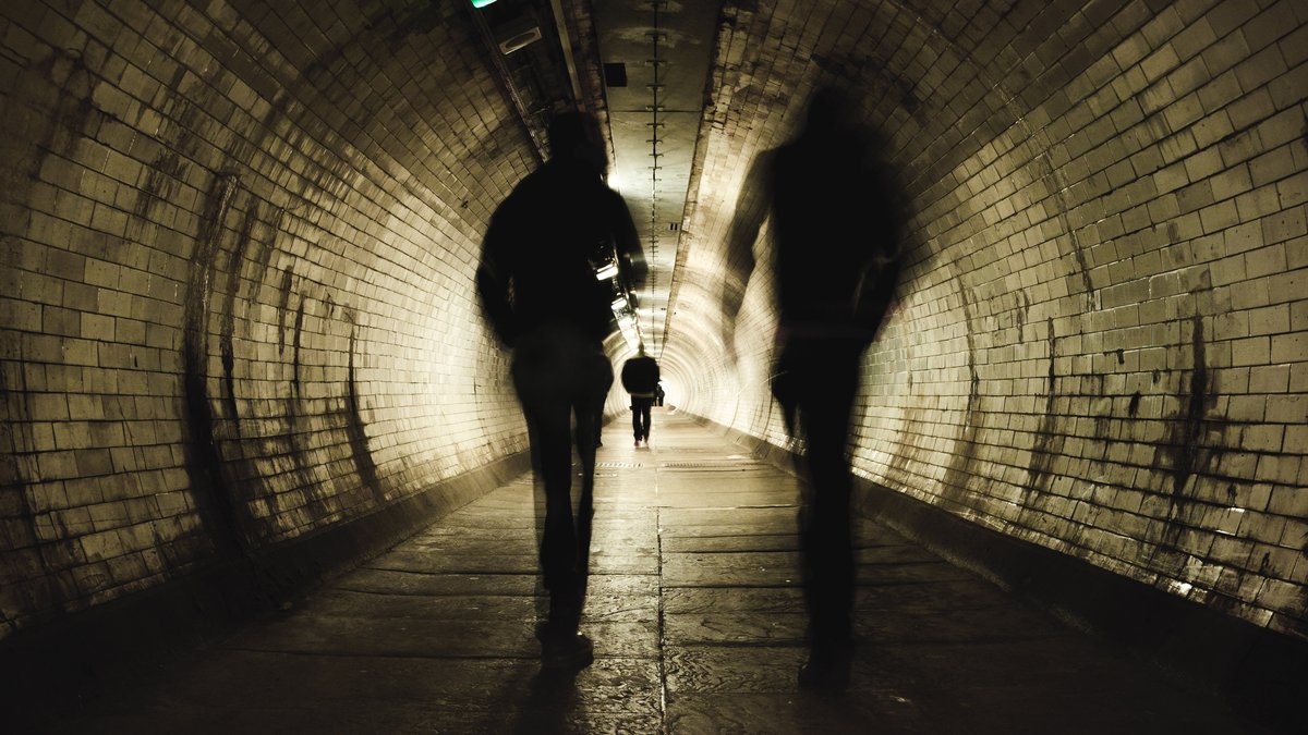 Symbolbild: unscharf fotografierte Menschen in einem Tunnel.