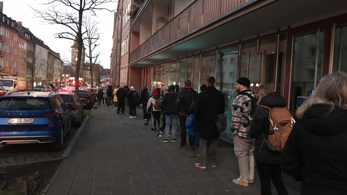 In einer Schlange vor dem Nürnberger Bürgeramt stehen viele Menschen auf dem Gehsteig. 
