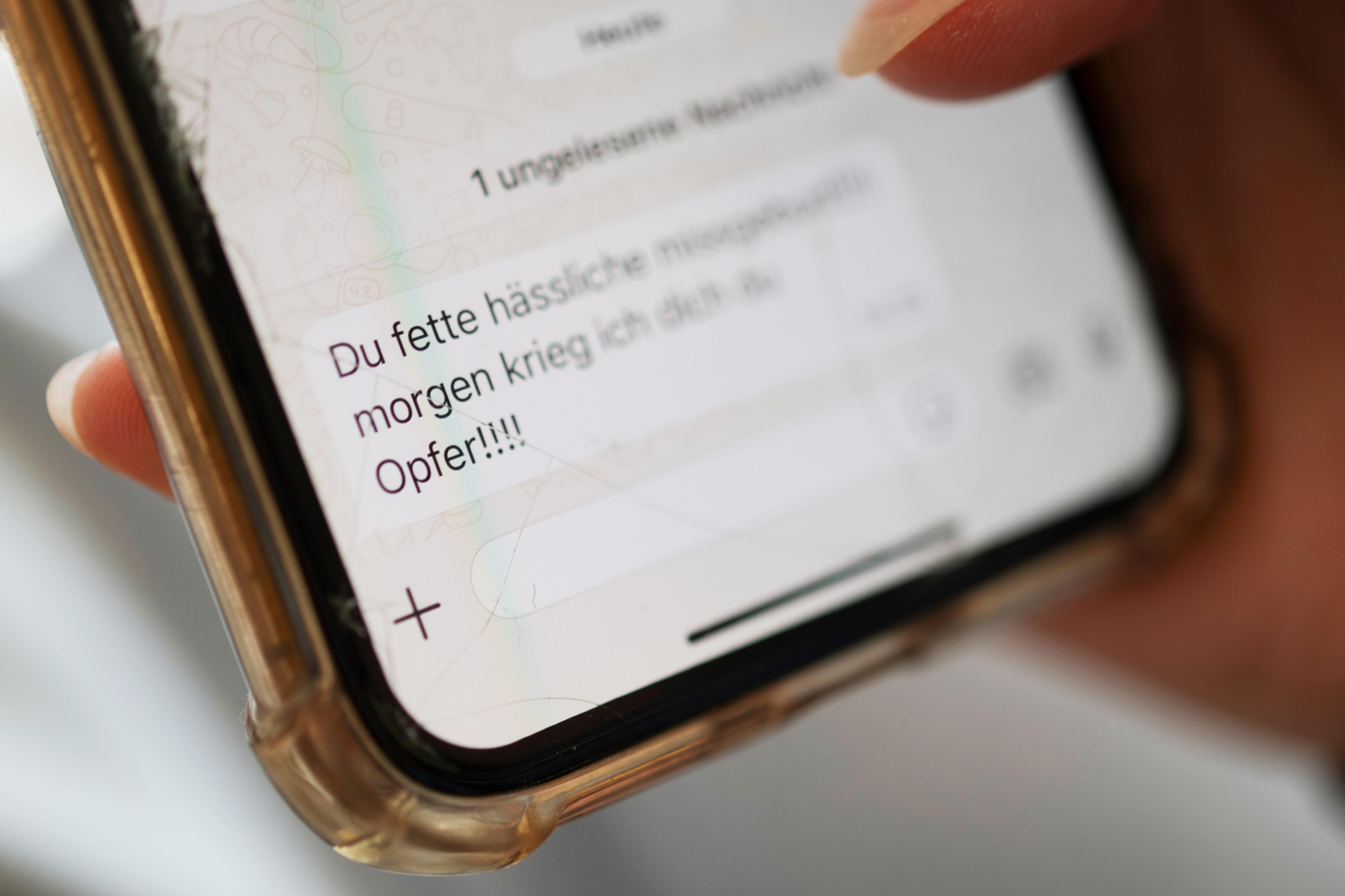 Hassnachrichten sind auf dem Display eines Smartphones zu sehen, das von einer Frau gehalten wird.