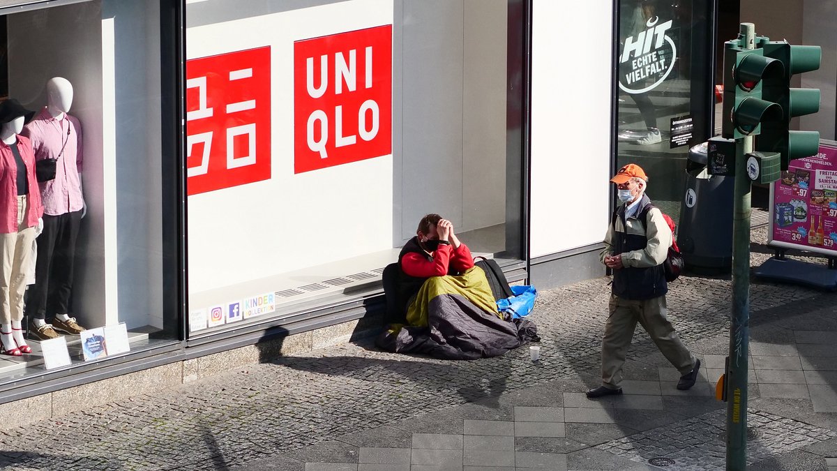 Ein Obdachloser mit Maske sitzt auf der Straße vor einem Geschäft.