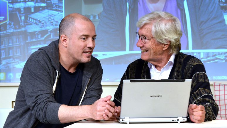 Zwei Männer am Tisch vor einem silbernen Laptop | Bild:Kajo Meyer/Komödie im Bayerischen Hof