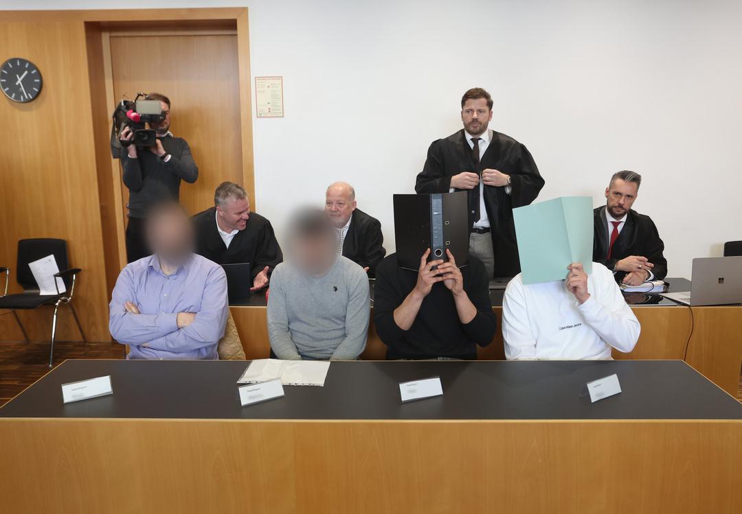 Der Hauptangeklagte (vorne r) sitzt in einem Gerichtssaal neben weiteren Angeklagten auf der Anklagebank. Er muss sich wegen Herbeiführung einer Sprengstoffexplosion und gefährlicher Körperverletzung verantworten. Der Mann soll am 11. November 2023 während des Bundesligaspiels des FC Augsburg gegen TSG 1899 Hoffenheim im Gästeblock einen in Deutschland nicht zugelassenen Böller gezündet haben. 