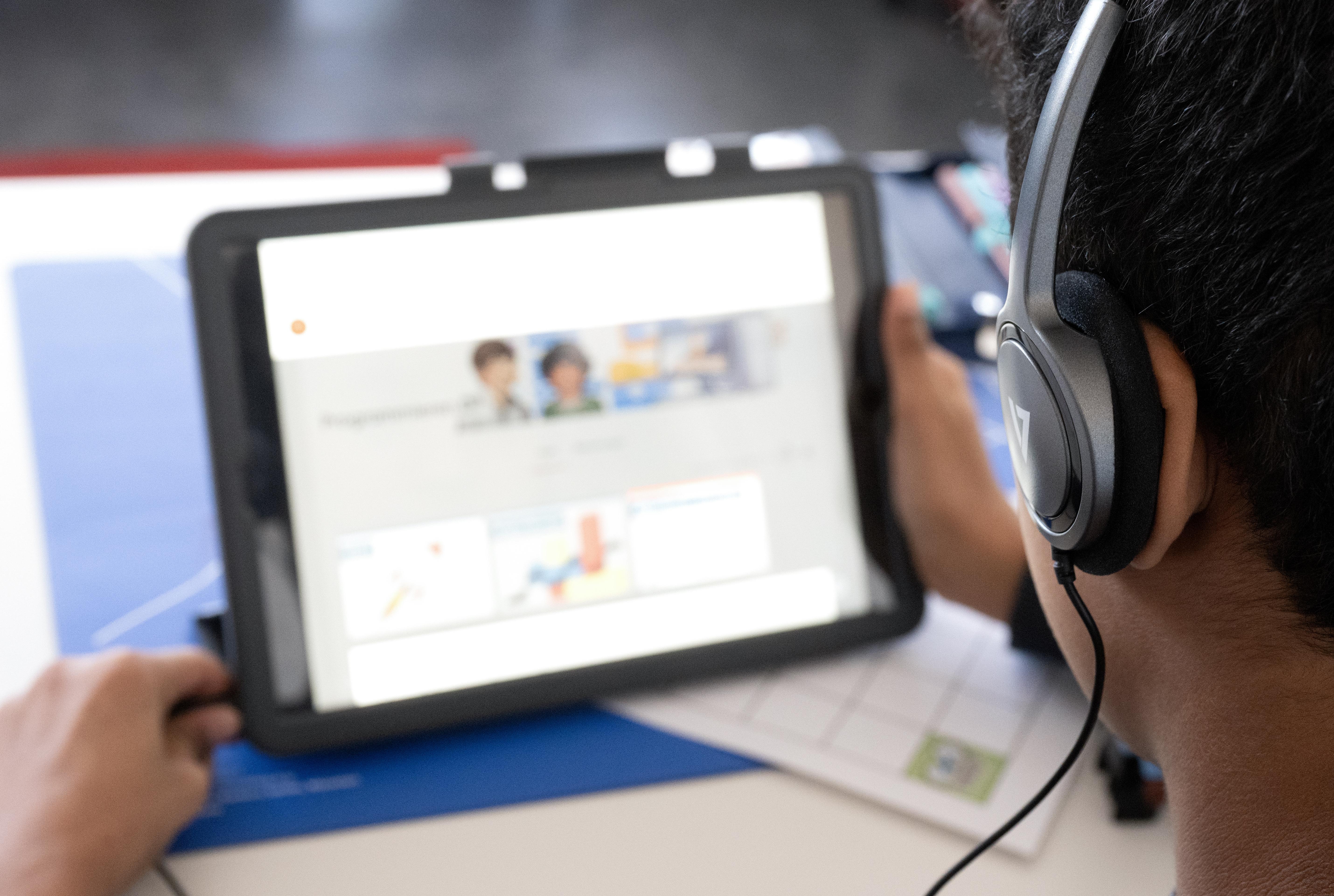 Ein Junge einer Deutschklasse sitzt vor einem Tablet.  