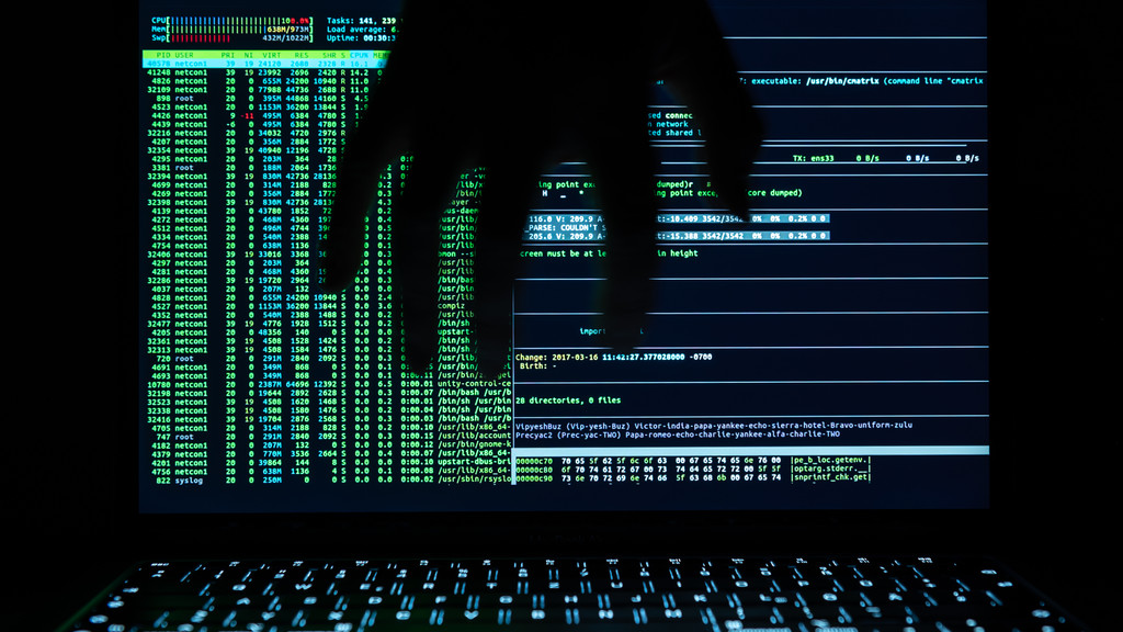 Eine Hand ist als Silhouette vor einem Hackerprogramm auf einem Laptop zu sehen.