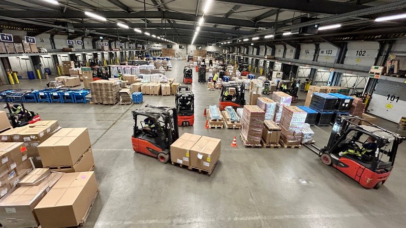 Gabelstapler fahren mit Paketen durch eine große Logistikhalle. | Bild: BR24/Ina Schwandner Gabelstapler fahren mit Paketen durch eine große Logistikhalle.
