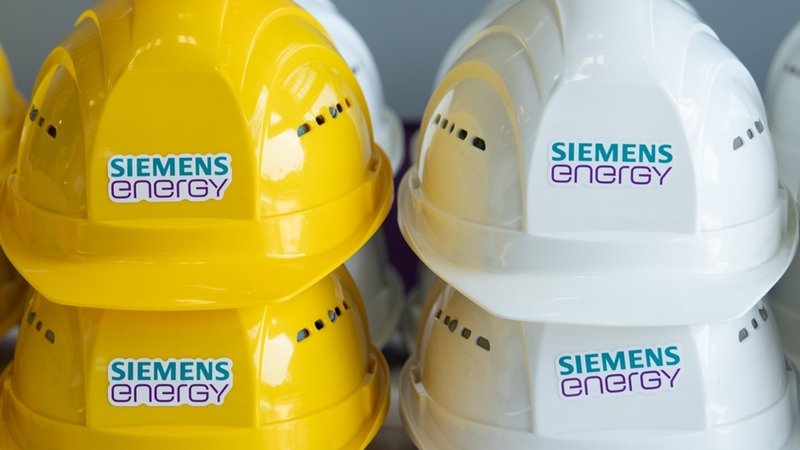Schutzhelme mit der Aufschrift "Siemens Energy" liegen in einer Halle auf einem Tisch.