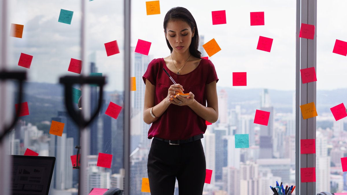 Eine junge Frau notiert etwas im Büro auf einen Notizblock.
