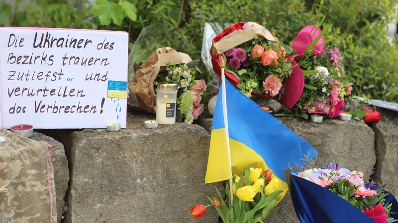 28.04.2024, Bayern, Murnau: Am Gelände eines Einkaufszentrums, an dem am Samstagabend (27.04.2024) zwei Männer aus der Ukraine getötet worden sind, wurden Blumen niedergelegt, sowie eine kleine ukrainische Flagge aufgestellt. Die Polizei konnte einen Mann festnehmen, der als dringend tatverdächtig gilt. Es handelt sich dabei um einen 57 Jahre alten Russen. Foto: Constanze Wilz/dpa +++ dpa-Bildfunk +++