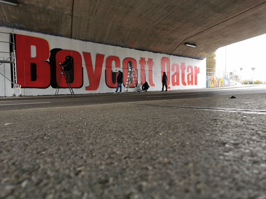 Vier Personen sprayen mit Hilfe von Leitern den Schriftzug "Boycott Qatar" auf die Wand der Graffiti-Unterführung im Süden Ingolstadts. 