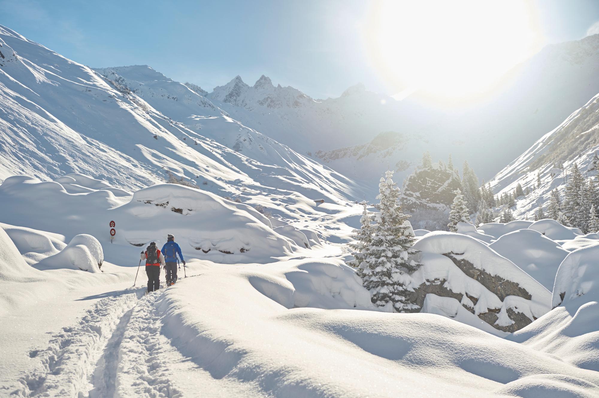 Zwei Menschen laufen durch hohen Schnee in den Schweizer Bergen