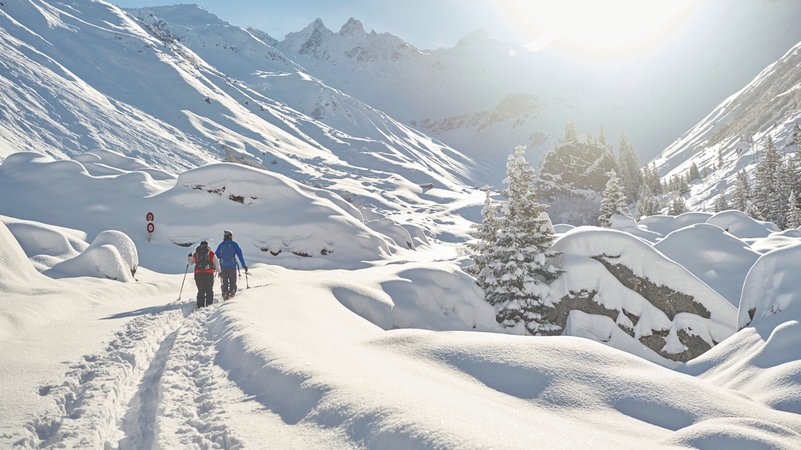Zwei Menschen laufen durch hohen Schnee in den Schweizer Bergen