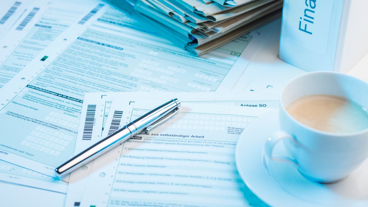 Unterlagen vom Finanzamt sowie ein Stift, ein Ordner und eine Tasse Kaffee stehen beziehungsweise liegen auf einem Tisch.