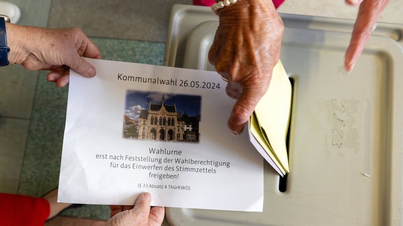 Eine Frau steckt bei den Kommunalwahlen in Thüringen in einem Wahllokal ihre Wahlzettel in die Wahlurne.