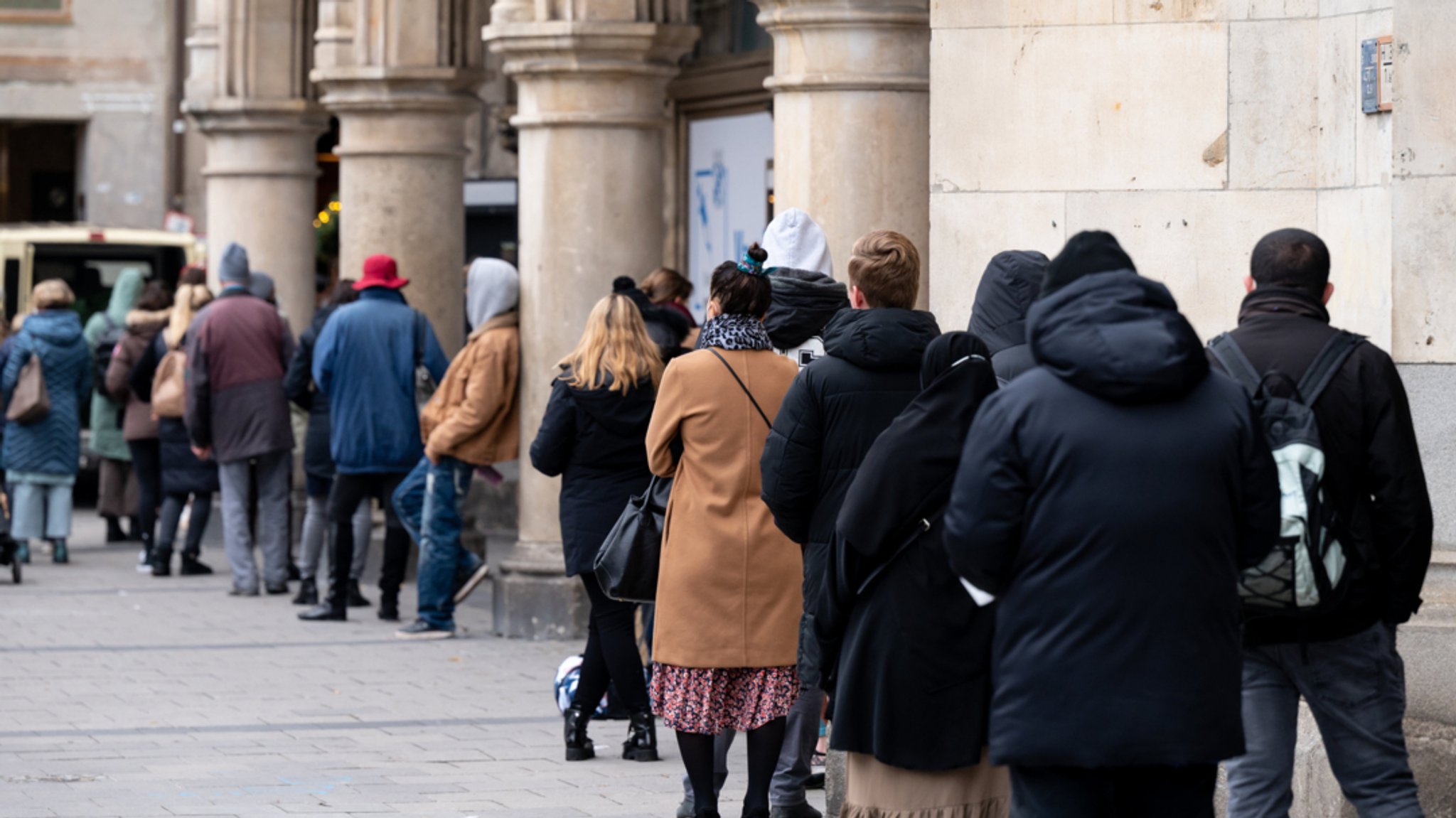 Zahlreiche Menschen stehen vor einem Impfzentrum in der Münchner Innenstadt in einer Warteschlange.